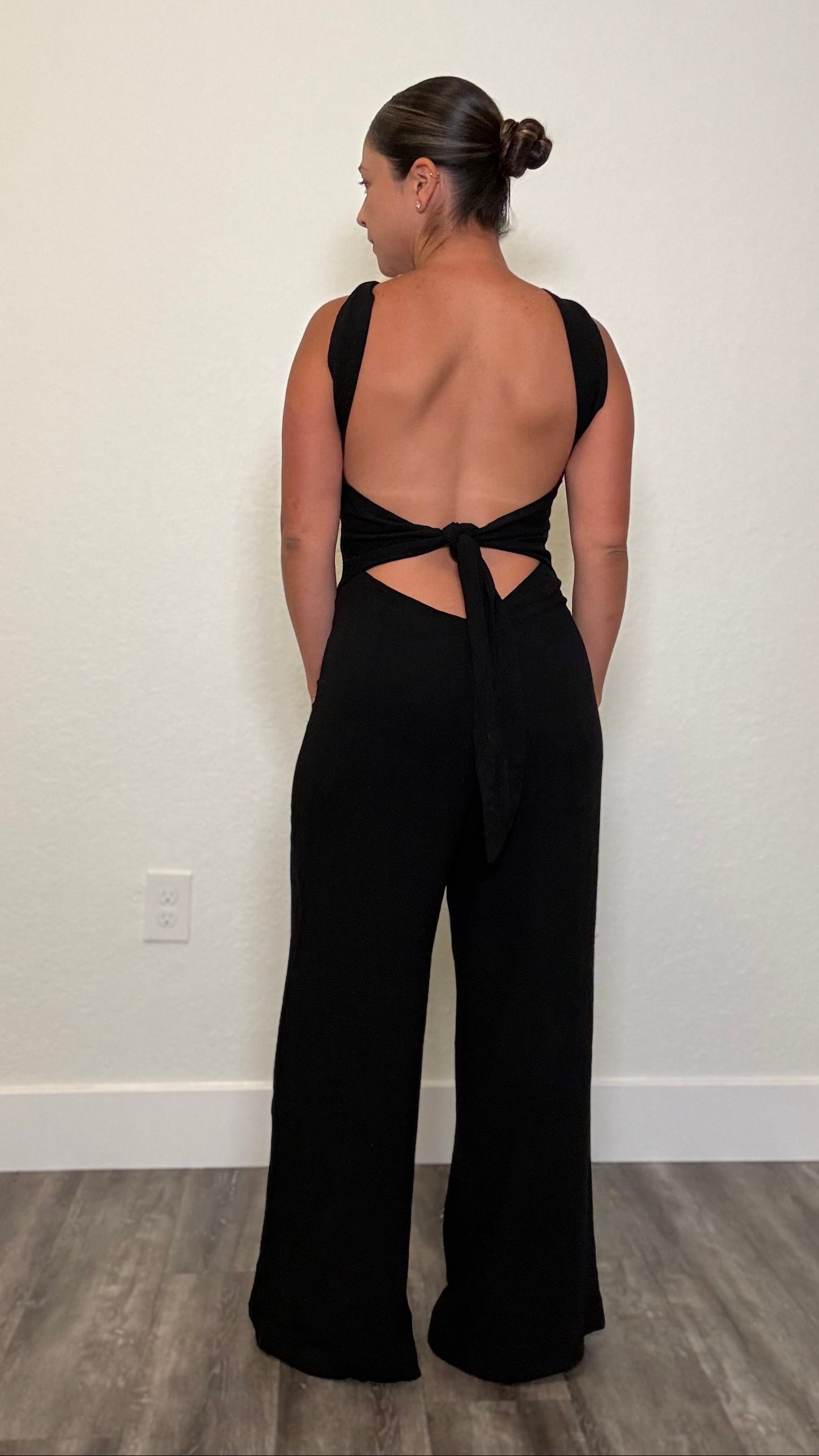 Woman wearing a black jumpsuit with open back and bow tie detail