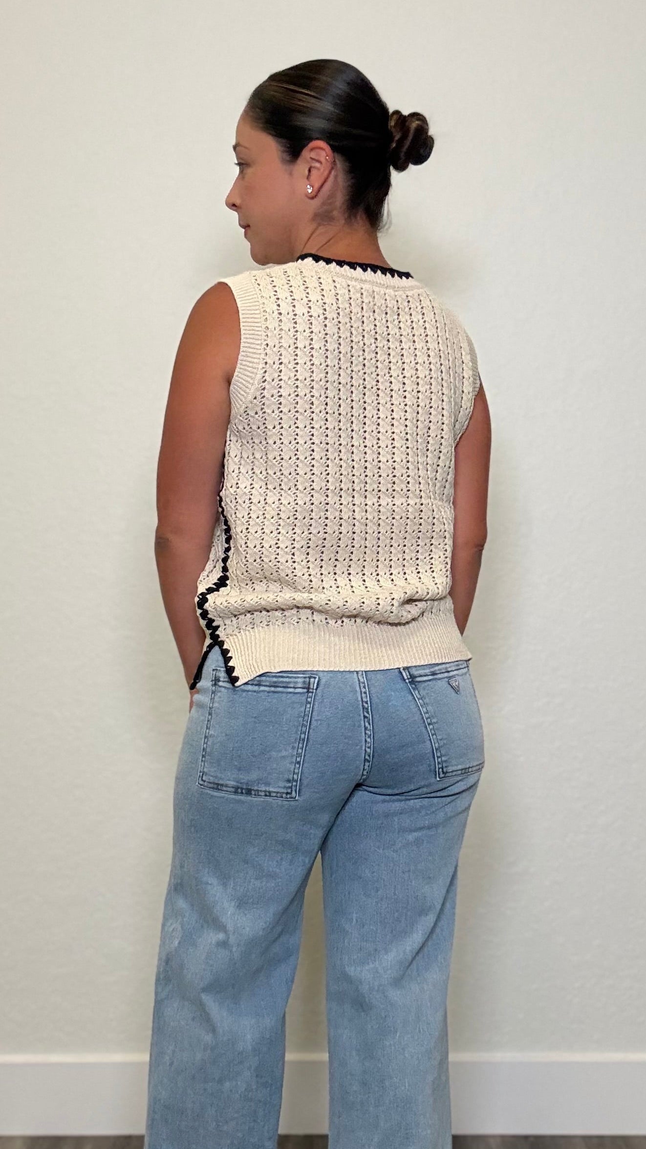 Woman wearing a sleeveless cream whipstitch top with black detailing along the sides