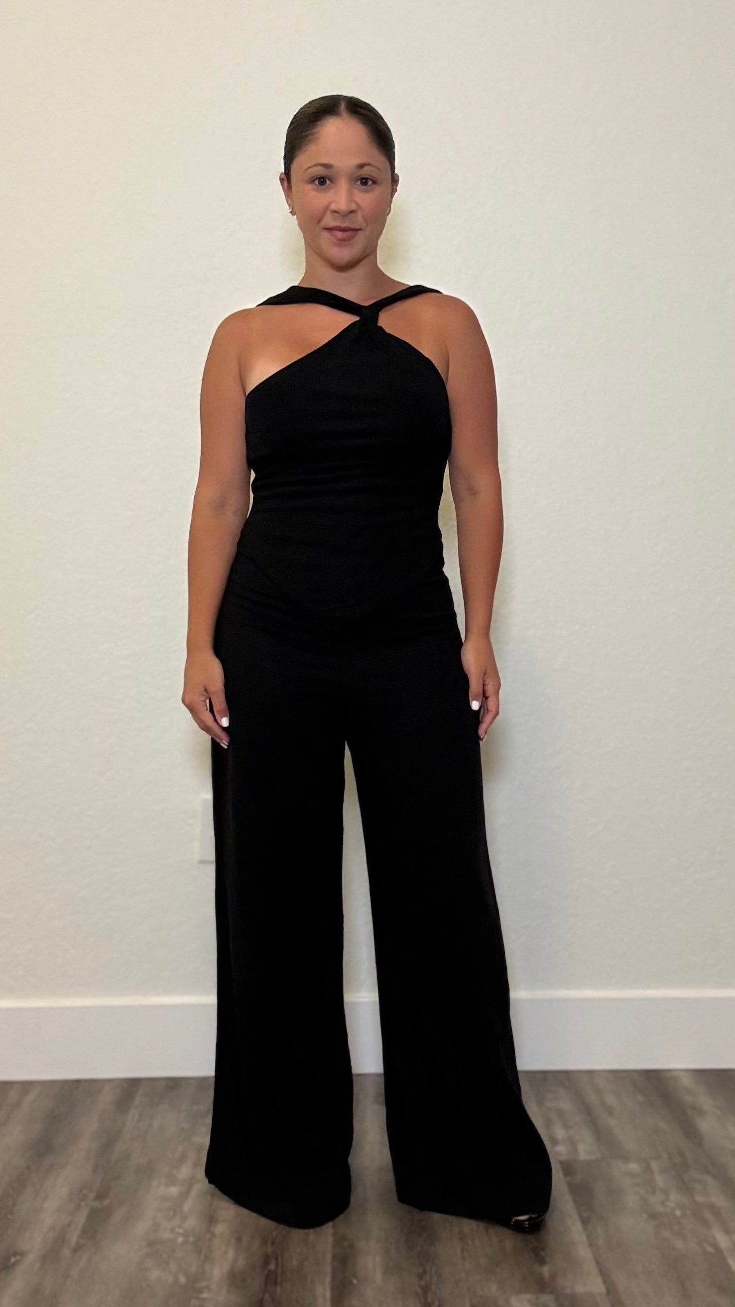 Woman wearing a black jumpsuit with knot detail around neck