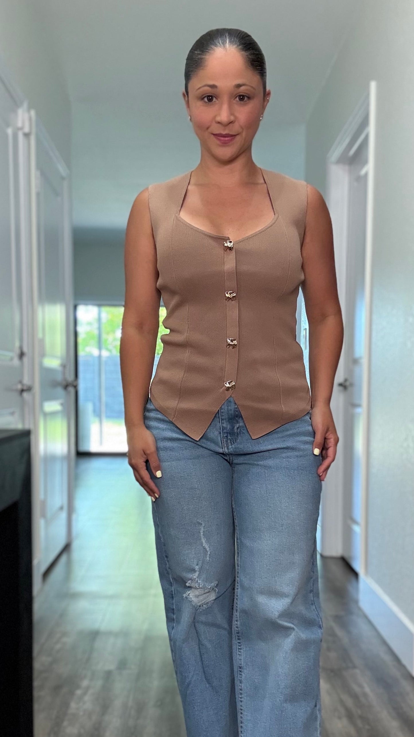 A sleeveless tan colored knit shirt with gold button details and bottom slit