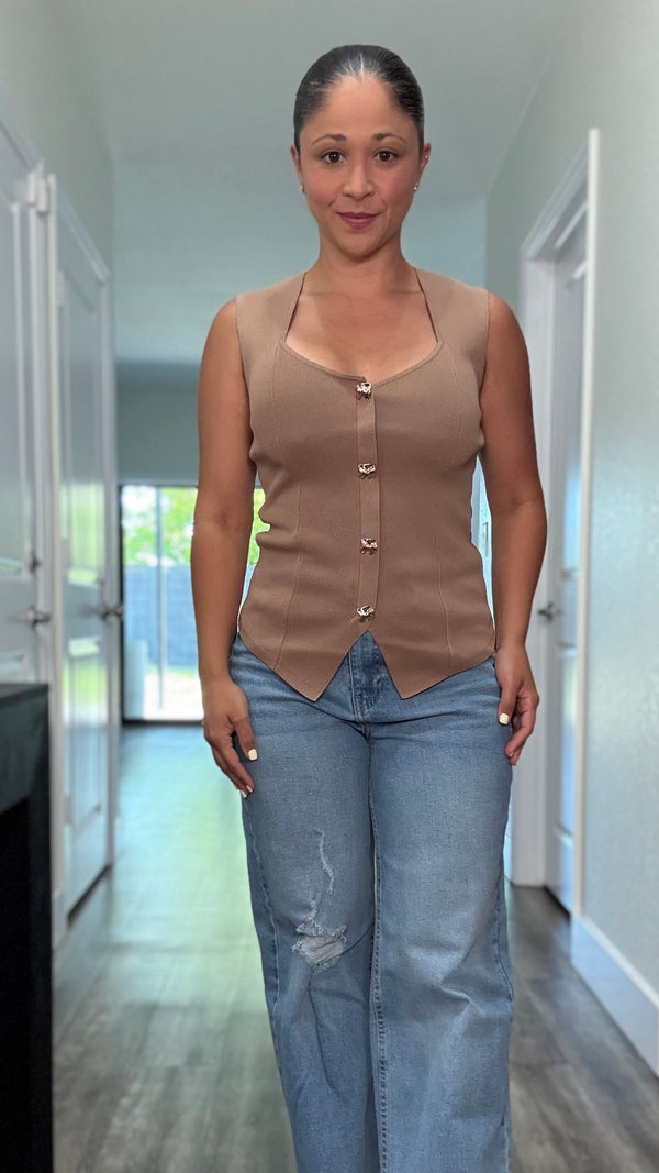 A sleeveless tan colored knit shirt with gold button details and bottom slit