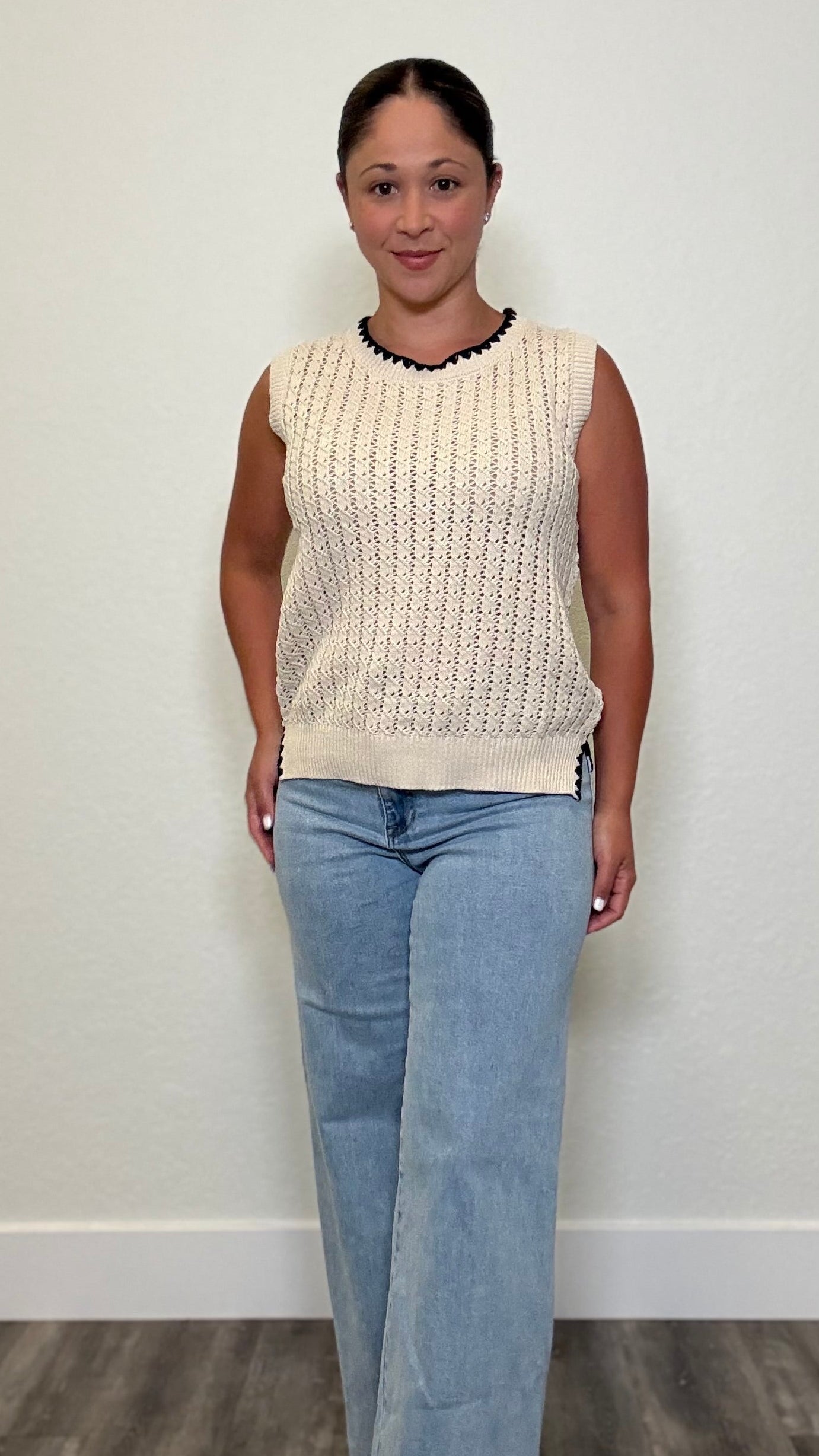 Woman wearing a sleeveless cream whipstitch top with black detailing around neckline