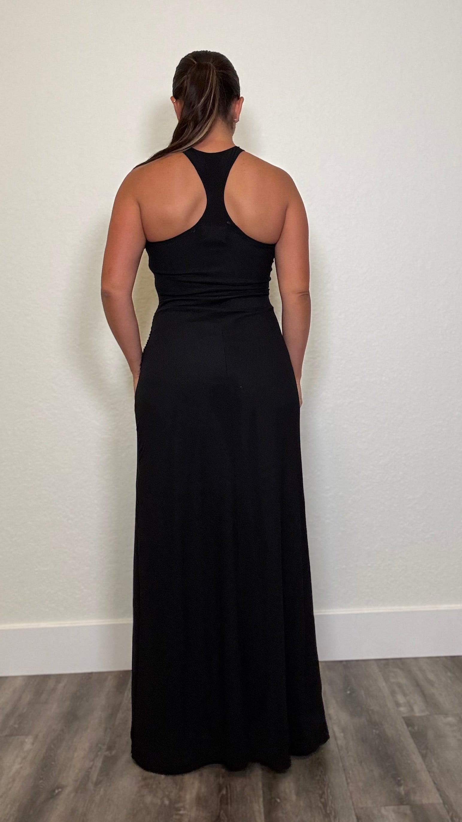 A woman viewed from behind wearing a black sleeveless maxi dress with a racerback.