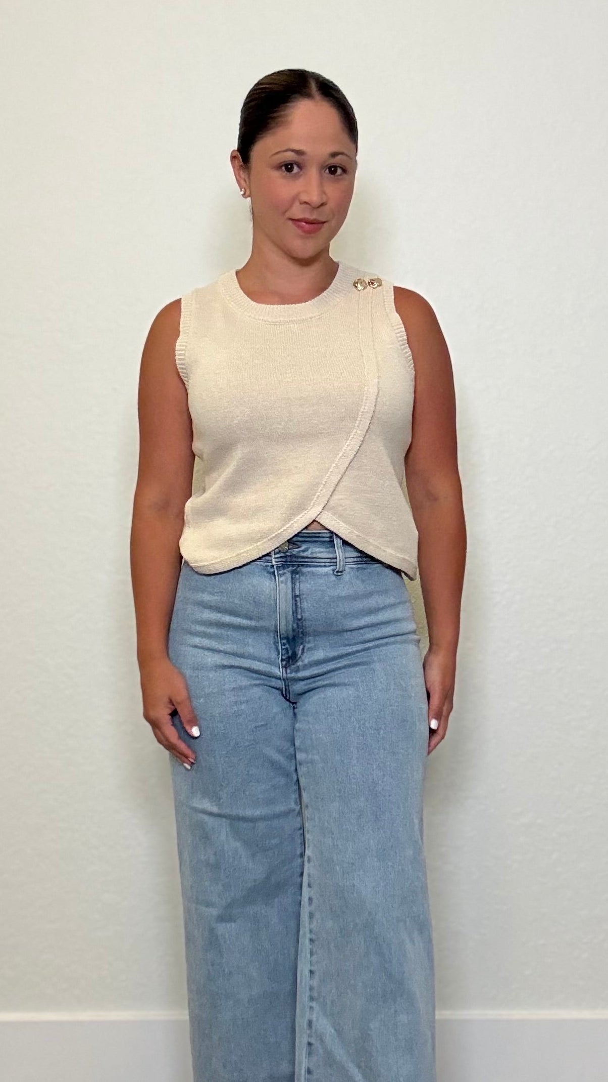 Woman wearing a beige wrap knit top with gold button details 