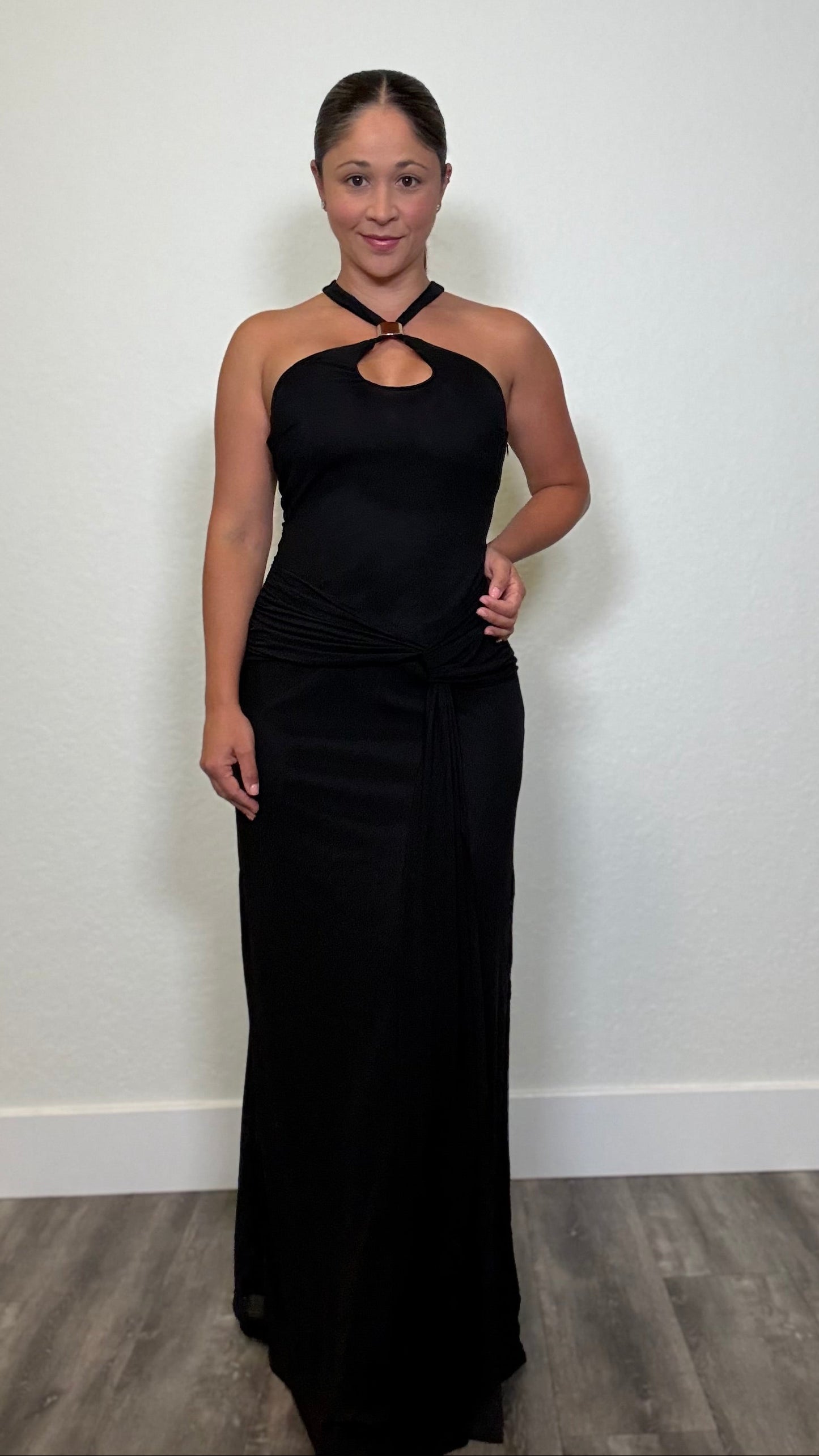 A woman modeling a black halter-neck maxi dress with a keyhole cutout at the chest and a draped waist